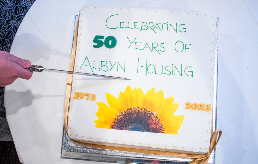 A picture of a cake being cut, it reads celebrating 50 years of Albyn Housing with a picture of a sunflower.